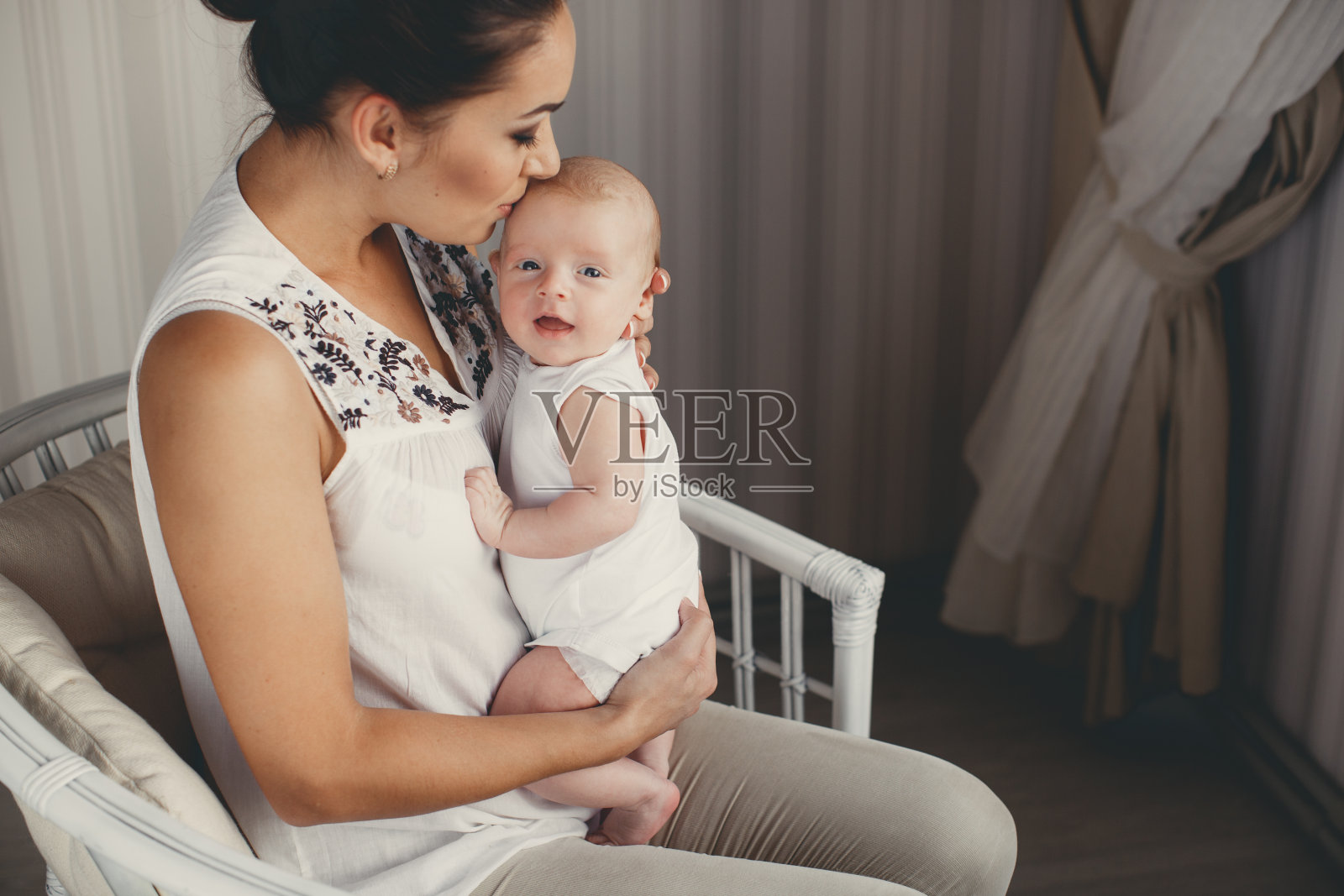 快乐的年轻母亲和刚出生的儿子在明亮的卧室里玩耍。照片摄影图片