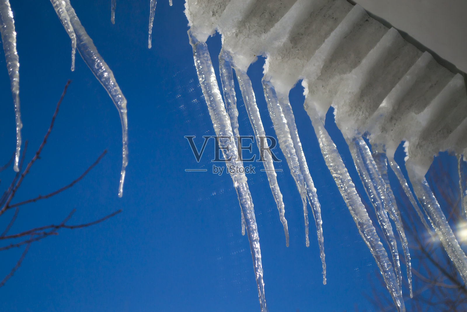 铁绿的屋顶上挂着冰柱，春天融雪。照片摄影图片