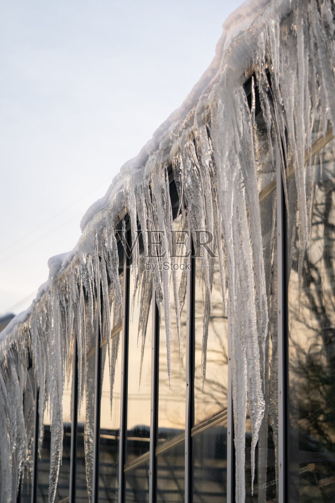 冬天屋顶和墙上挂着冰柱。在春天融化的冰雪中结冰的水融化了照片摄影图片