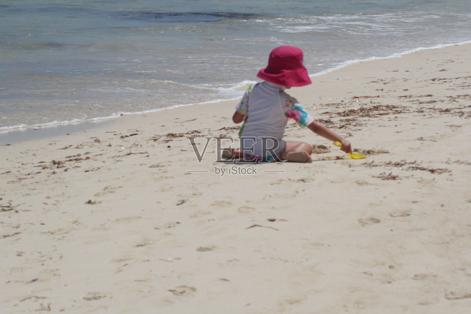 后景，一个孩子坐在海滩的岸边玩沙子照片摄影图片