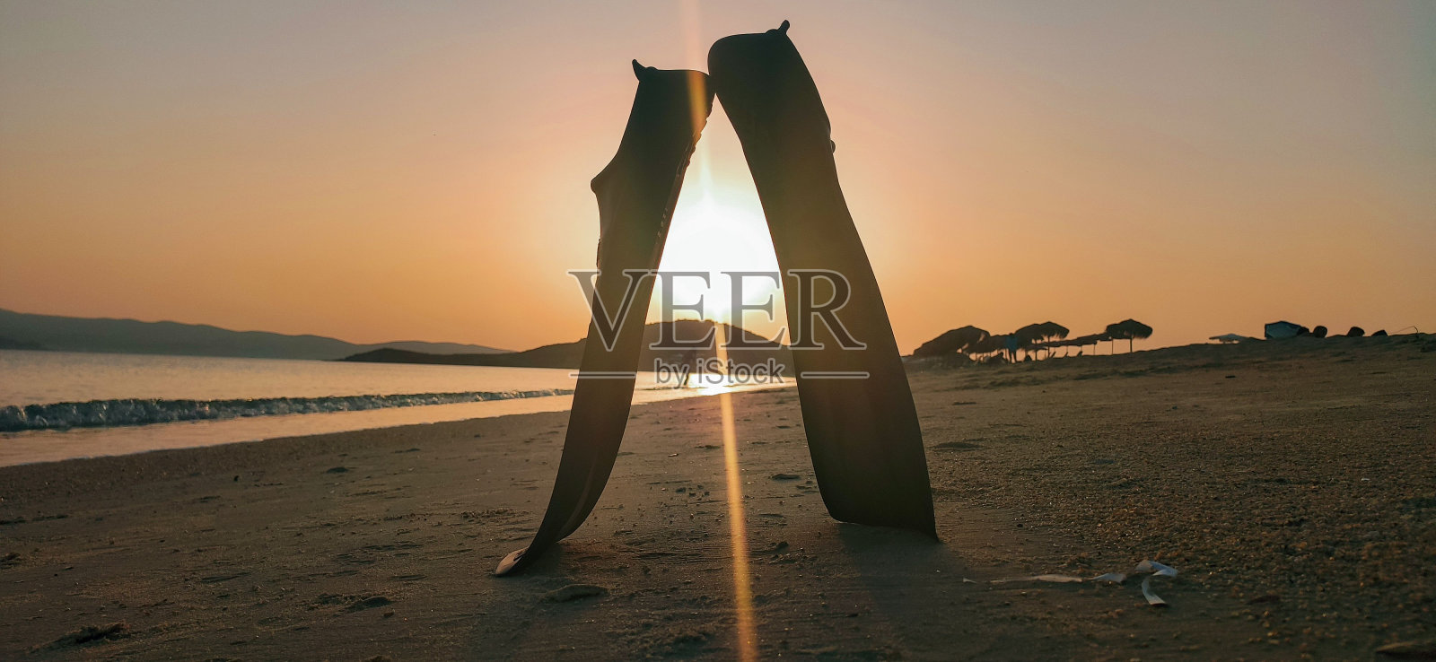 沙滩上的一双潜水鞋，背景是天空中明亮的日落照片摄影图片