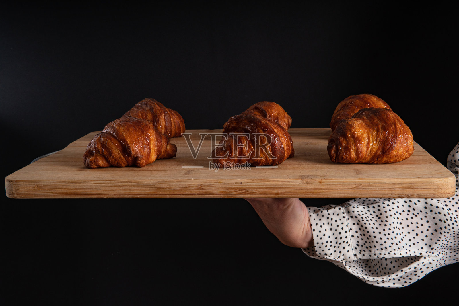 一只手拿着一块木板与羊角面包在黑色背景，正面视图，复制空间照片摄影图片