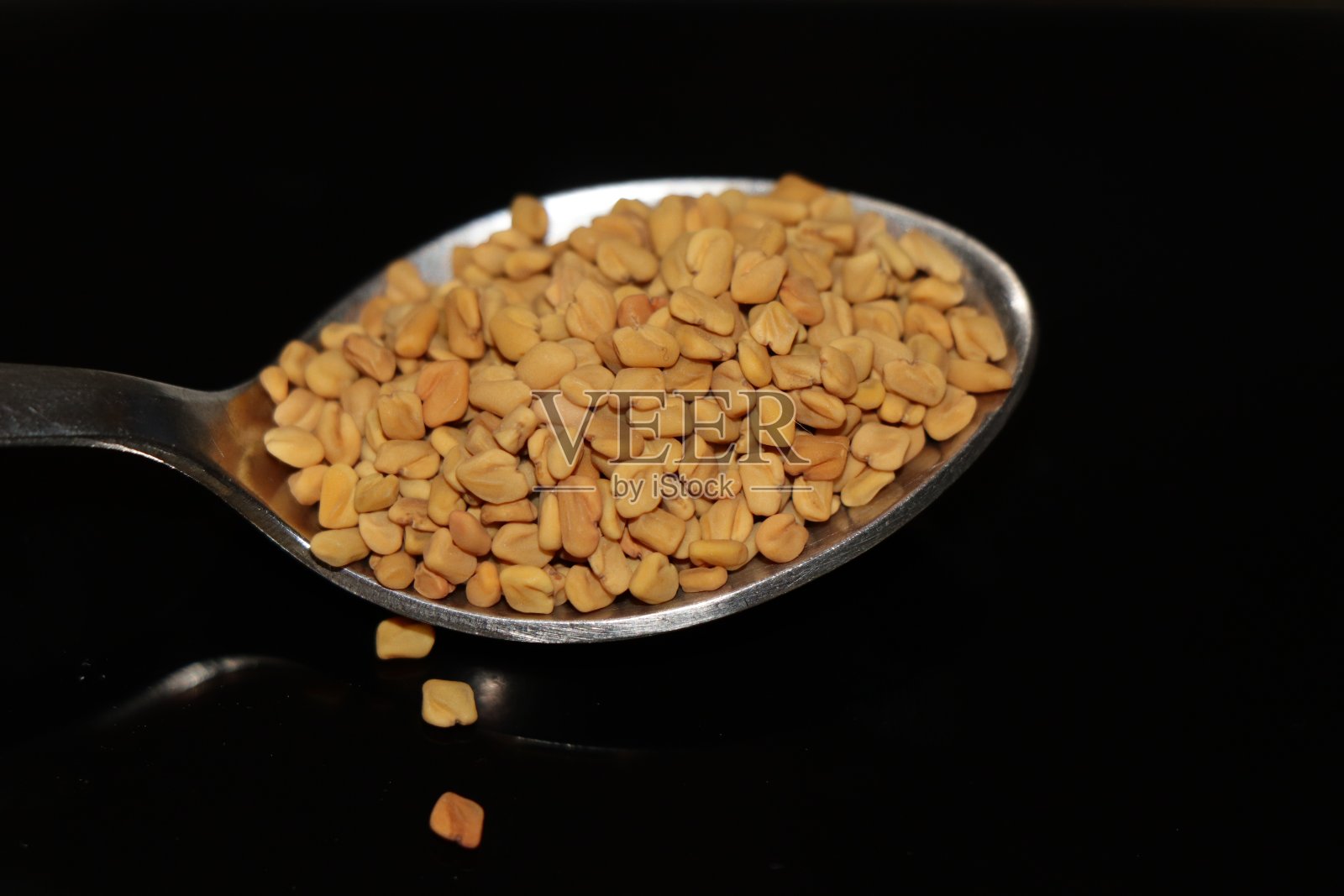 有机胡芦巴种子在勺子上黑色背景。胡芦巴的创意形象。混合香料中的胡芦巴成分和食物中的调味剂。照片摄影图片