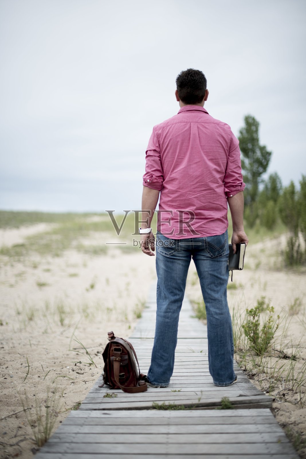 从后面垂直拍摄一个男人站在一条木小路上，手里拿着圣经照片摄影图片