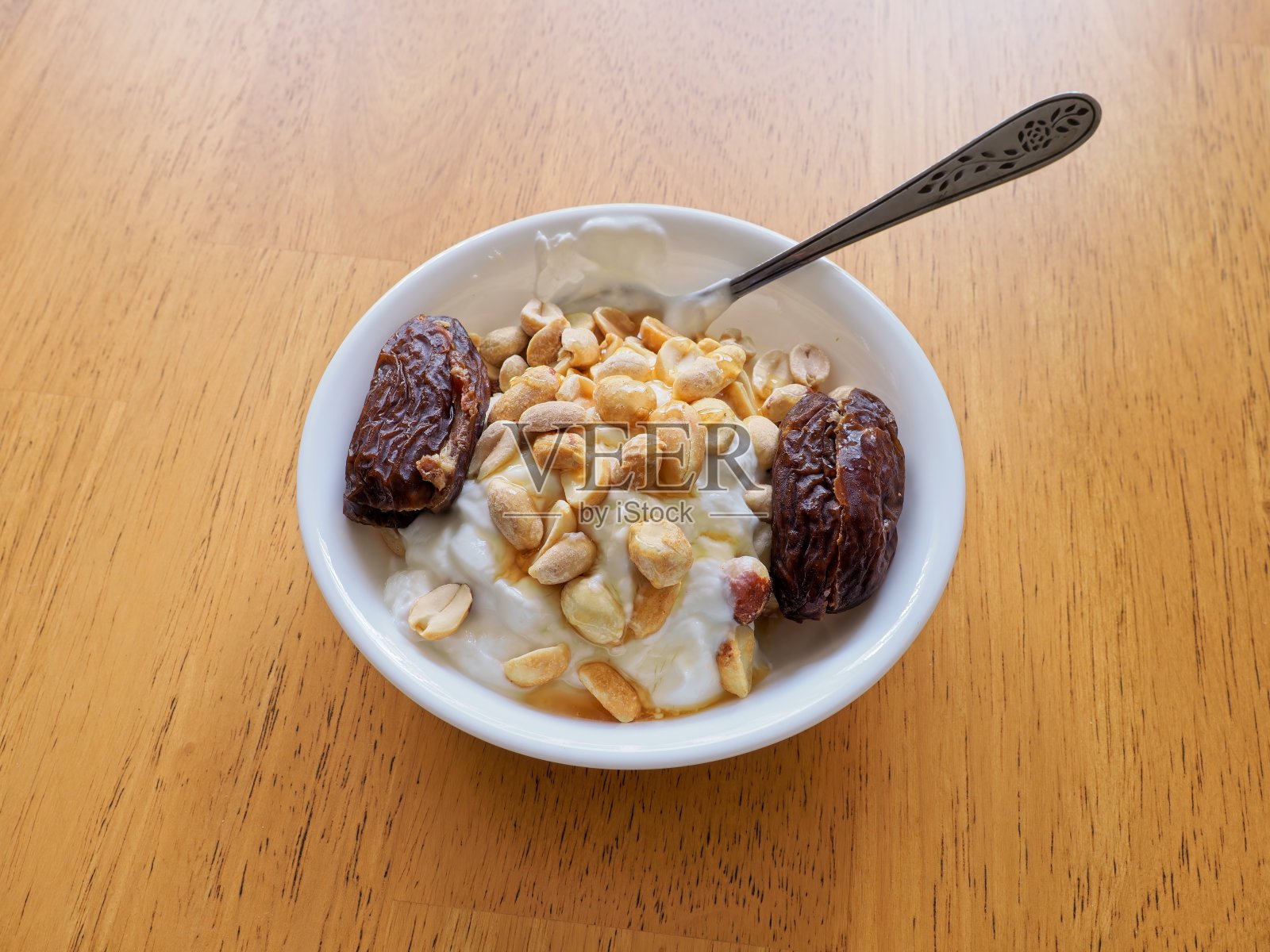 一种健康的颓废小吃，希腊酸奶配花生和去核枣，淋上蜂蜜照片摄影图片