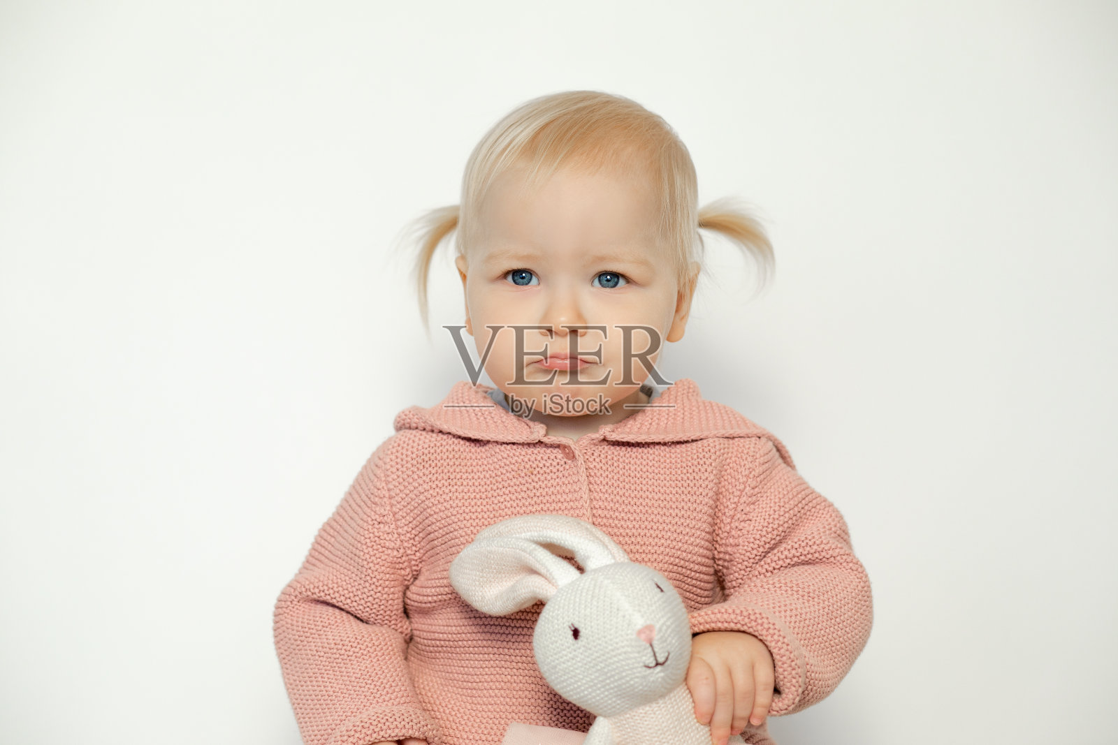 小女婴玩毛绒玩具孤立的白色。幼儿带着悲伤的表情抱着泰迪兔。金发碧眼，穿粉红色衣服，抱着一只兔子。复活节。节日礼物照片摄影图片