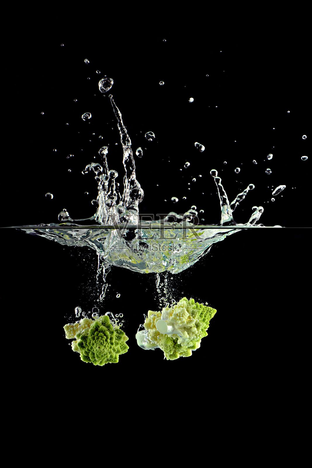 在黑色背景下，西兰花片落入水中溅起水花照片摄影图片