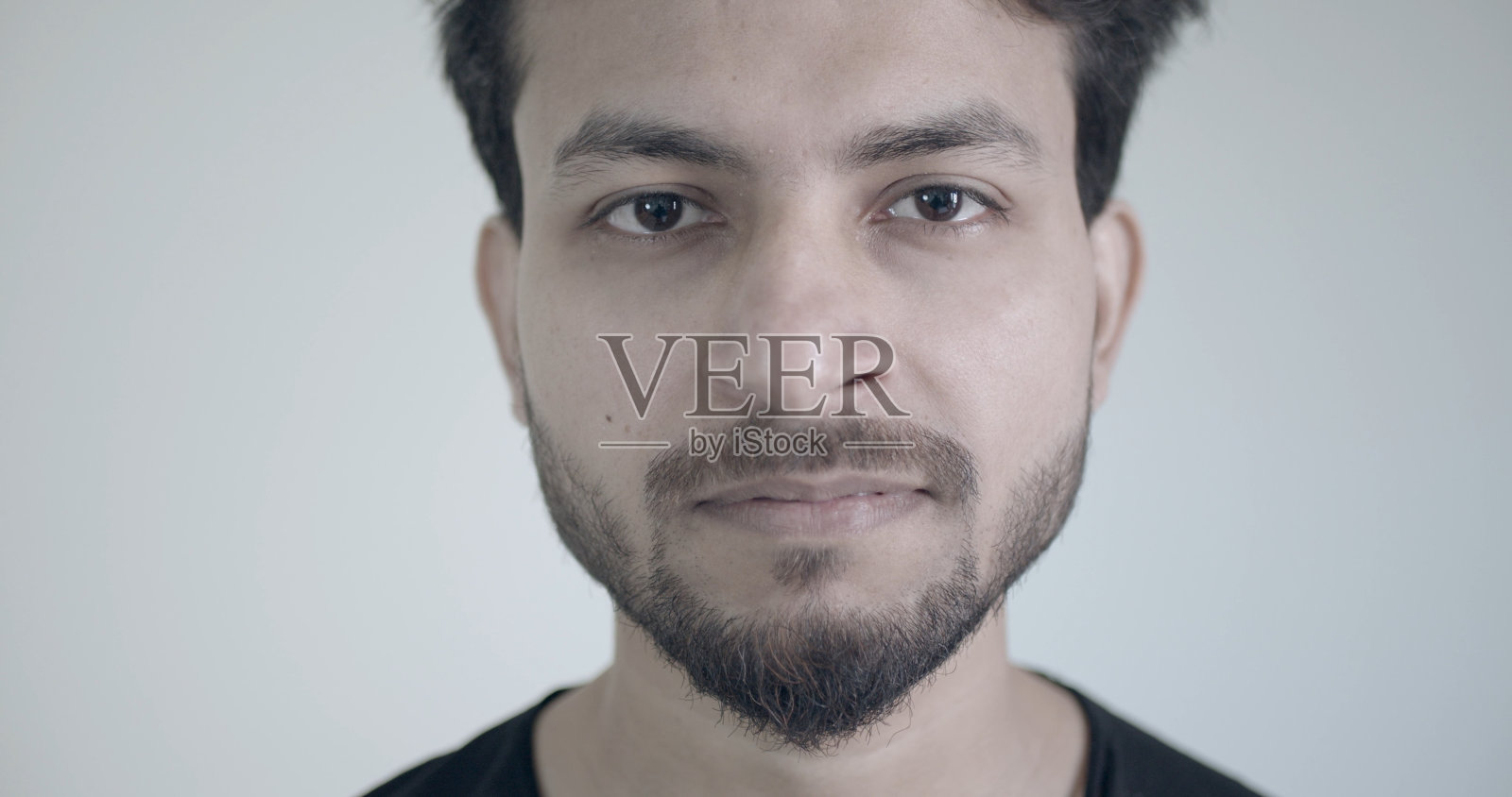 英俊的蓄着胡子的印度人在白色的墙壁背景上毫无表情地看着相机照片摄影图片