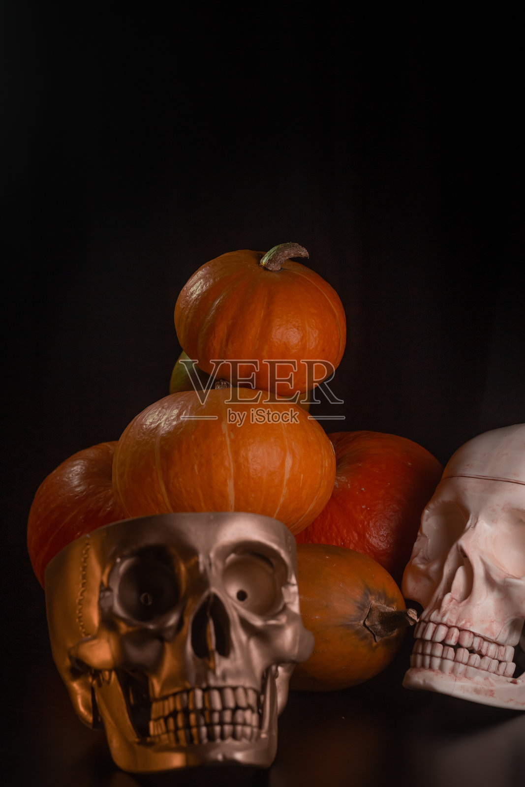 橙黄色的南瓜配上蜡烛和黑色背景上的骷髅头万圣节的概念和秋天收获的