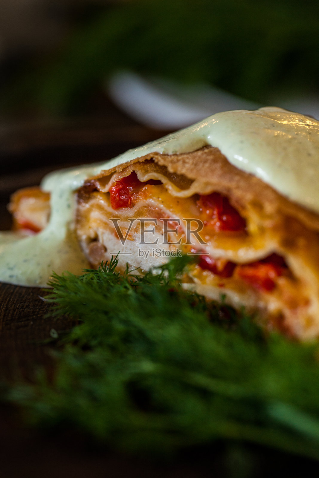 用鸡肉、番茄、酸奶油酱和香草做成的薄酥皮馅饼。躺在一个黑色的石板盘上。淋上酸奶油和香蒜沙司。一根莳萝小枝躺在馅饼附近和后面。照片摄影图片
