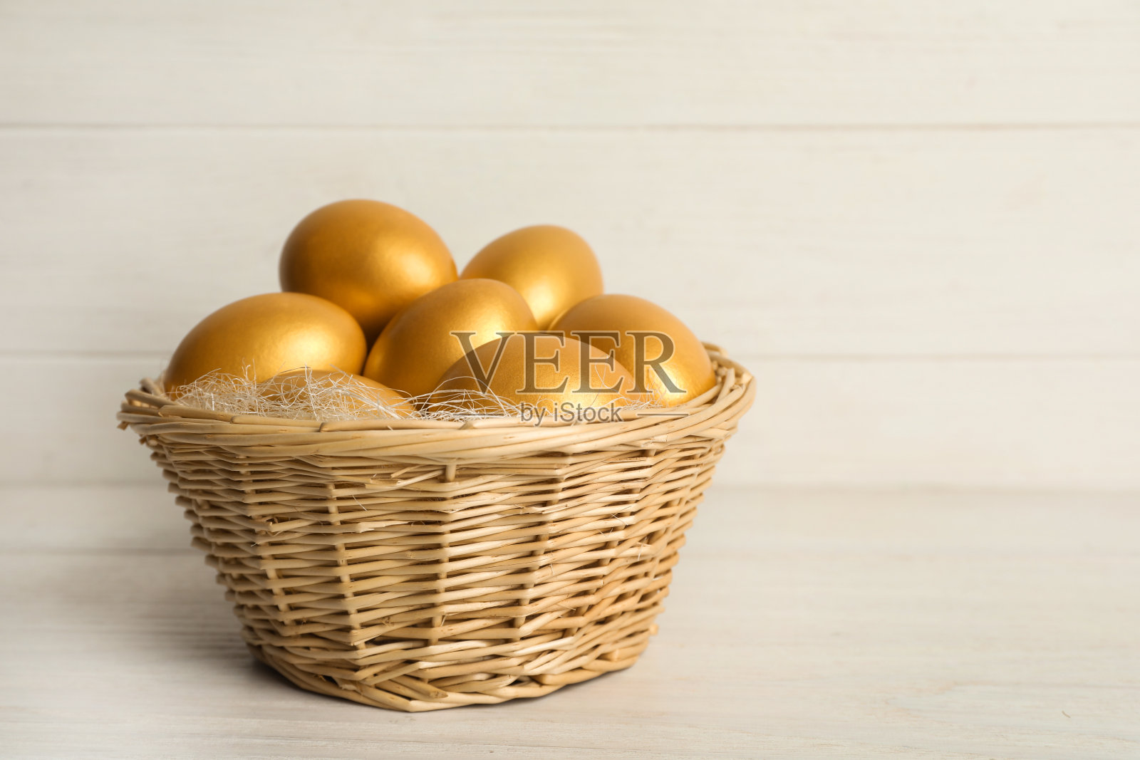 闪闪发光的金色鸡蛋在柳条篮子上的白色木桌，文字的空间照片摄影图片