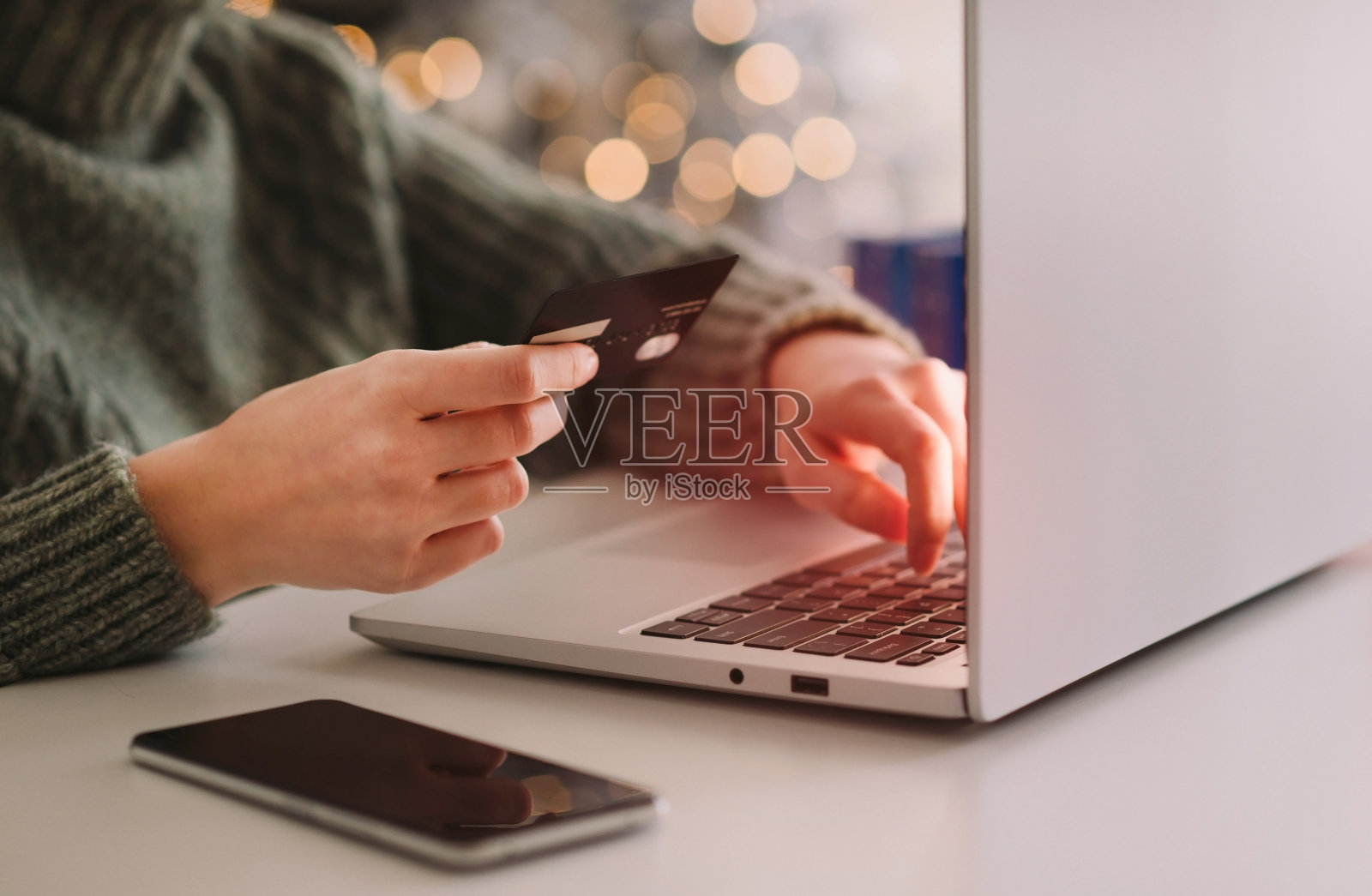 圣诞节网购，冬季打折促销，在家网购。女性的手放在笔记本电脑上，带有模糊的散景灯照片摄影图片