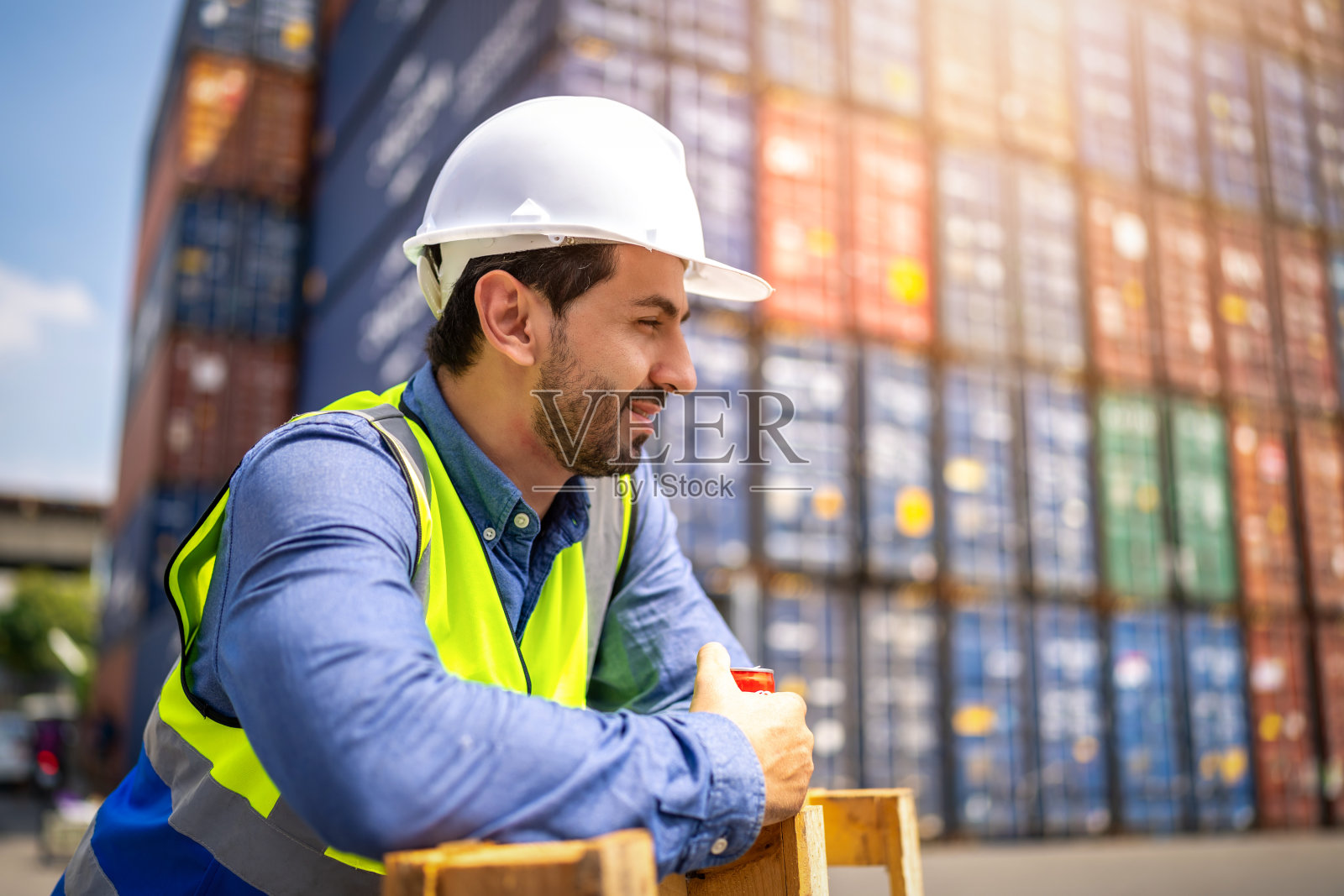 英俊的工程师或工头戴着个人防护装备在日落时检查集装箱存储与货物集装箱背景。物流全球进出口航运的产业概念。照片摄影图片