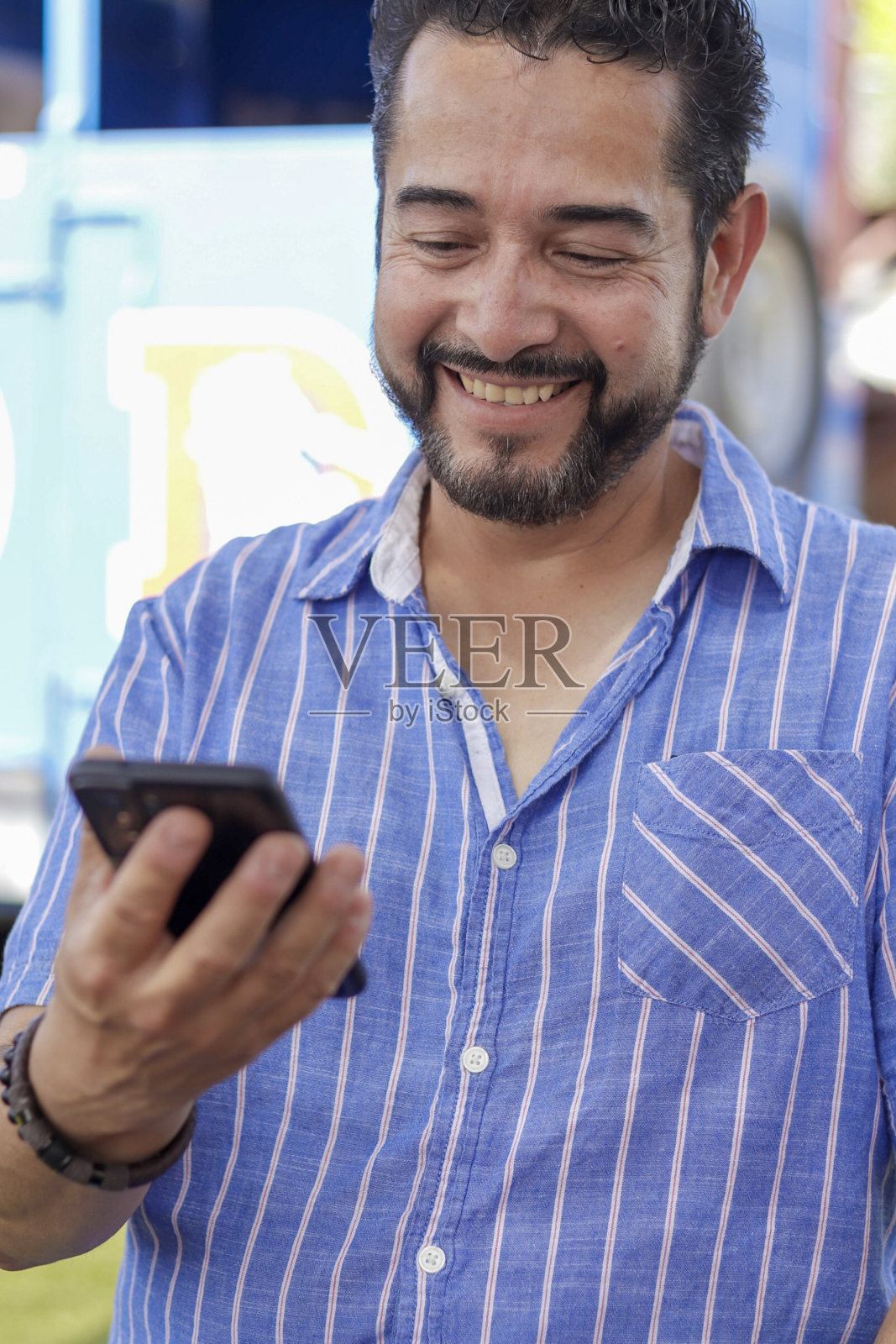 垂直拍摄的一个微笑的西班牙成年男子微笑着看他的手机照片摄影图片