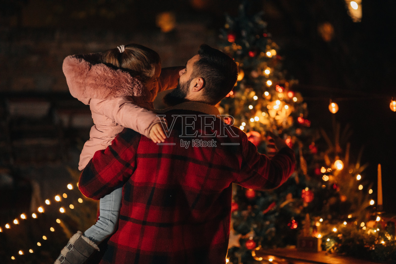 年轻的父亲抱着他的小女儿在圣诞树前照片摄影图片