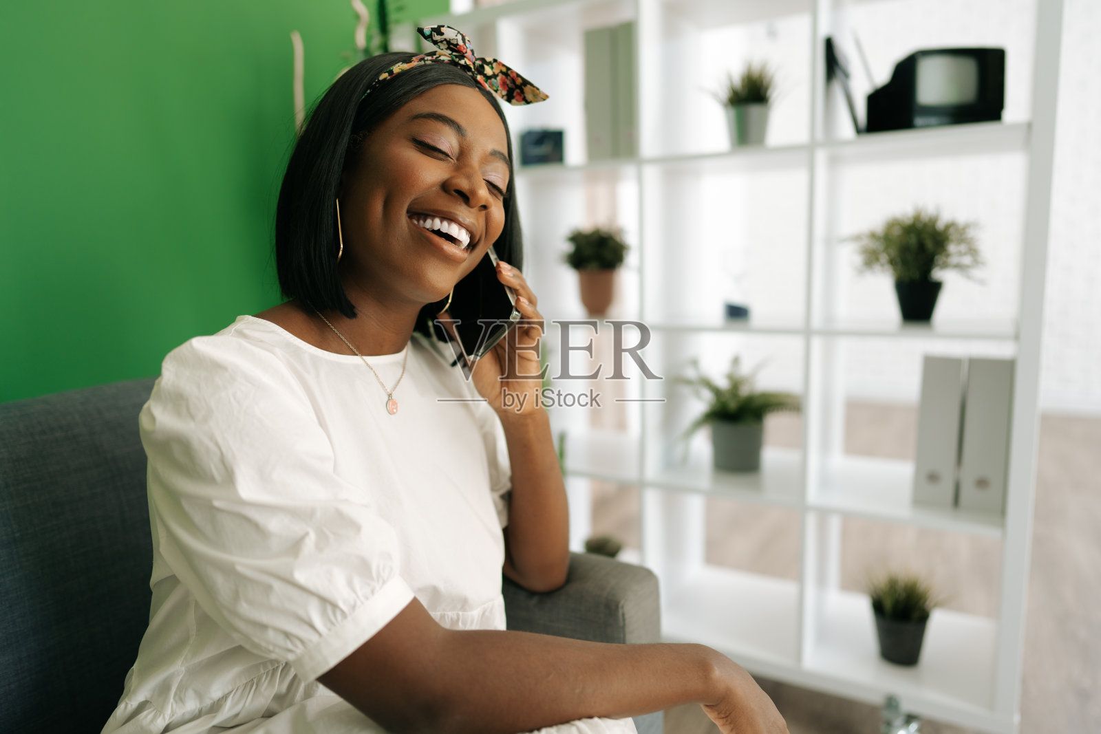 年轻的非洲妇女坐在家里的沙发上打电话照片摄影图片