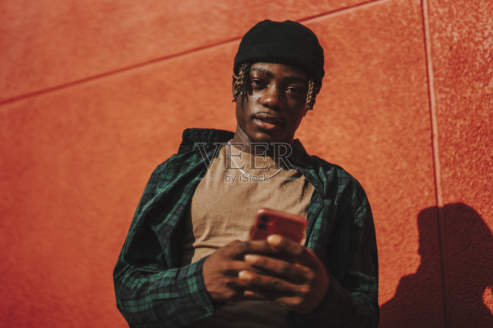 英俊时髦的西班牙男子拿着手机，在红墙背景上摆姿势照片摄影图片