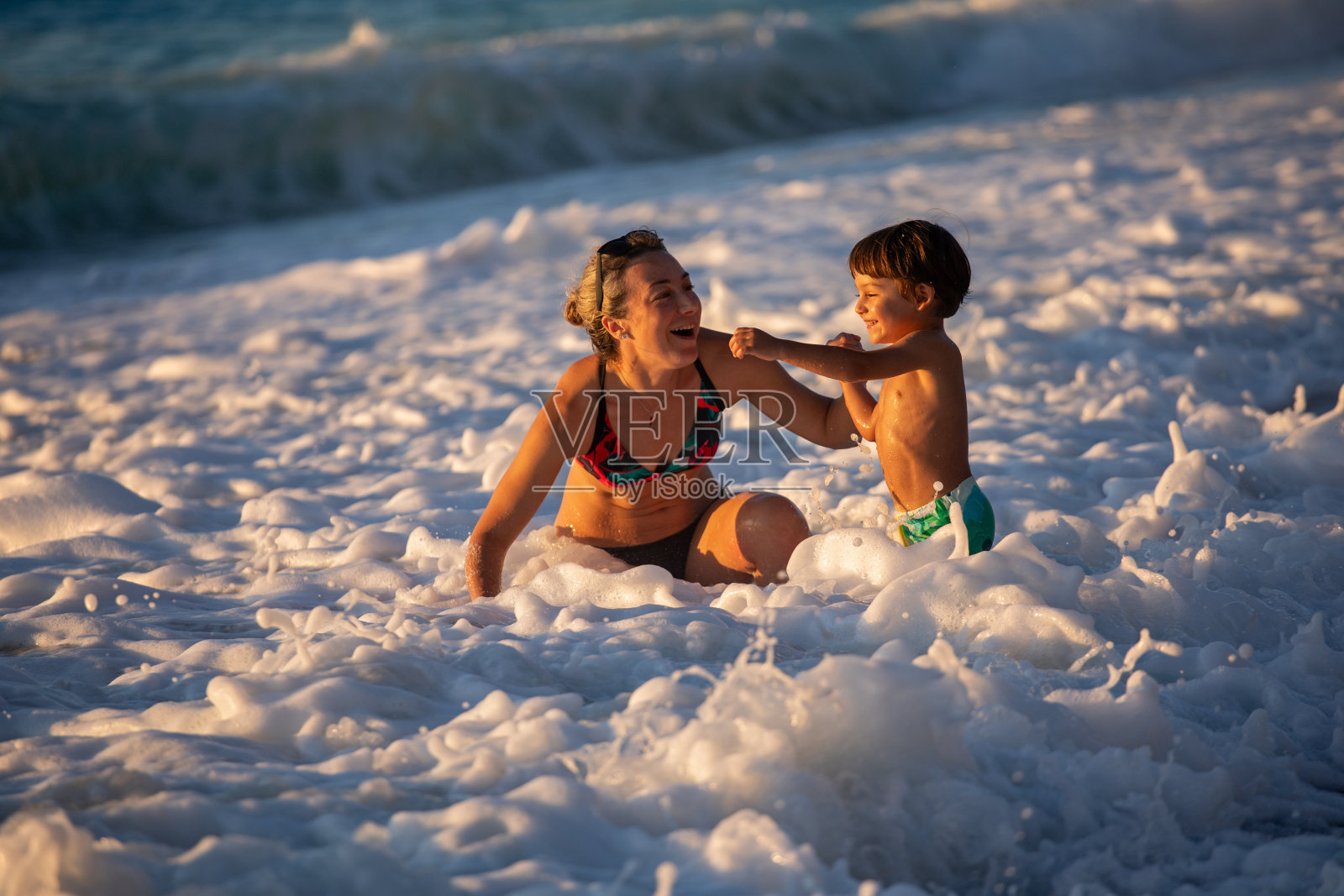 年轻的女人和她的孩子在浪花中玩耍照片摄影图片