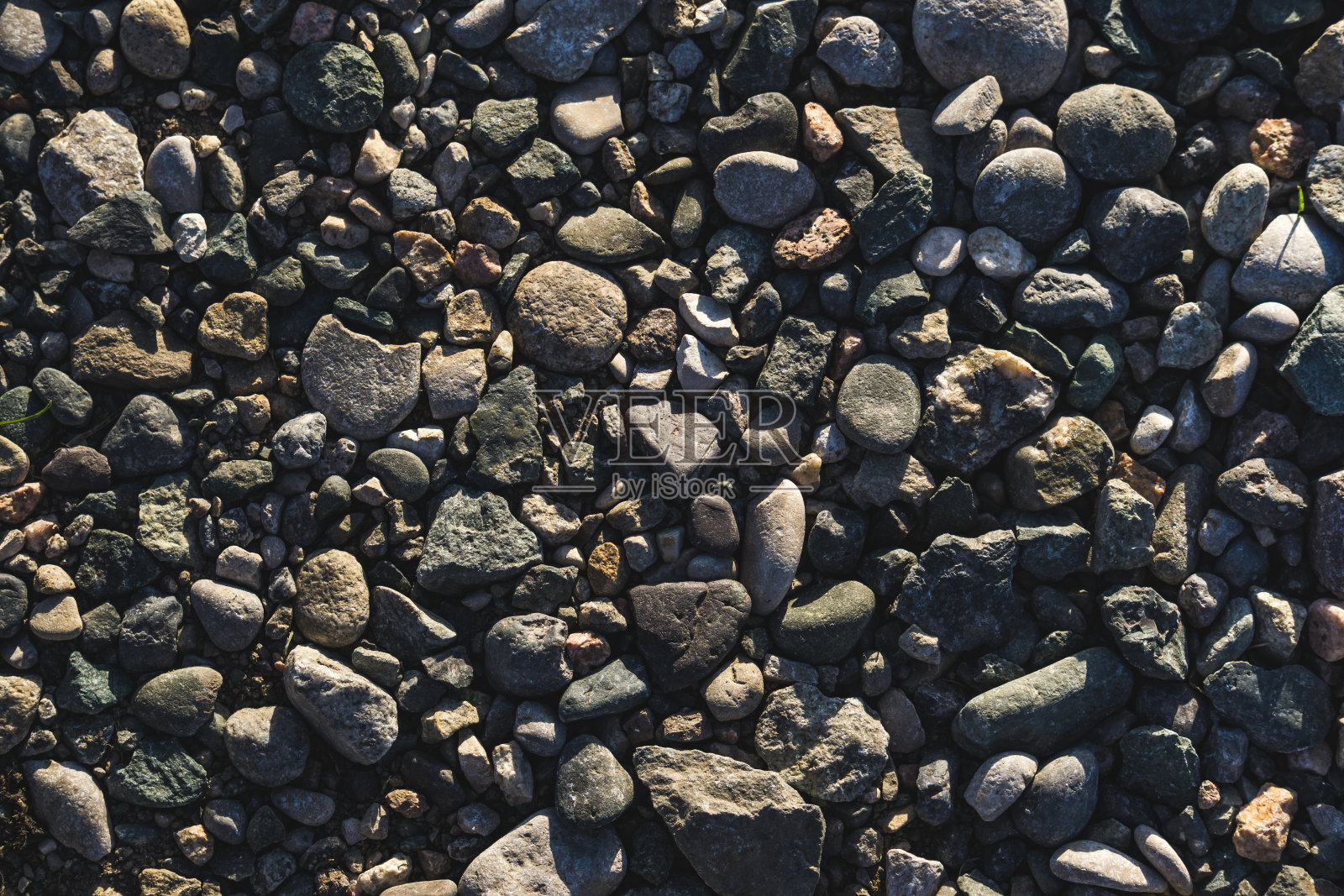 不同色调的鹅卵石质地被夕阳从侧面照亮，黑色抽象的鹅卵石为背景照片摄影图片