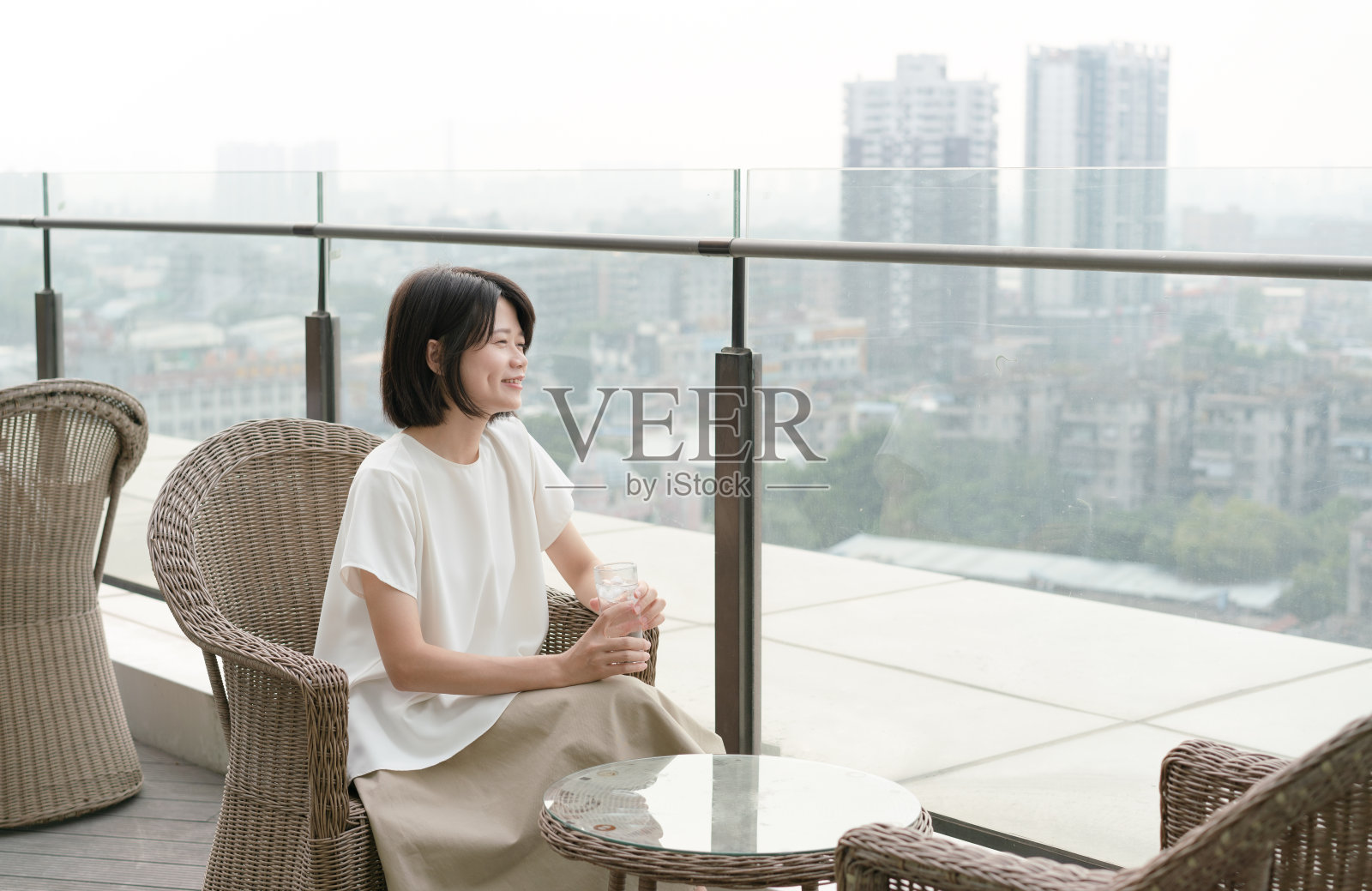 放松的女人坐在阳台上的椅子上，拿着一杯水照片摄影图片