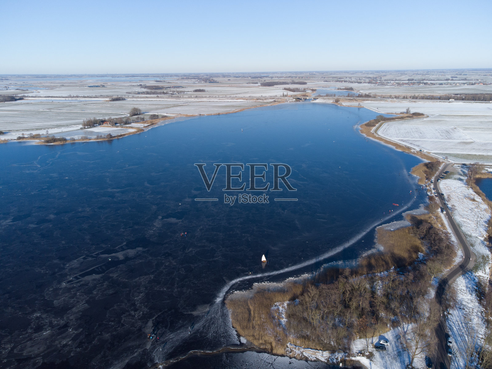 荷兰冬天结冰的湖面。蓝天映照在水面上，人们在结冰的水面上滑冰。照片摄影图片