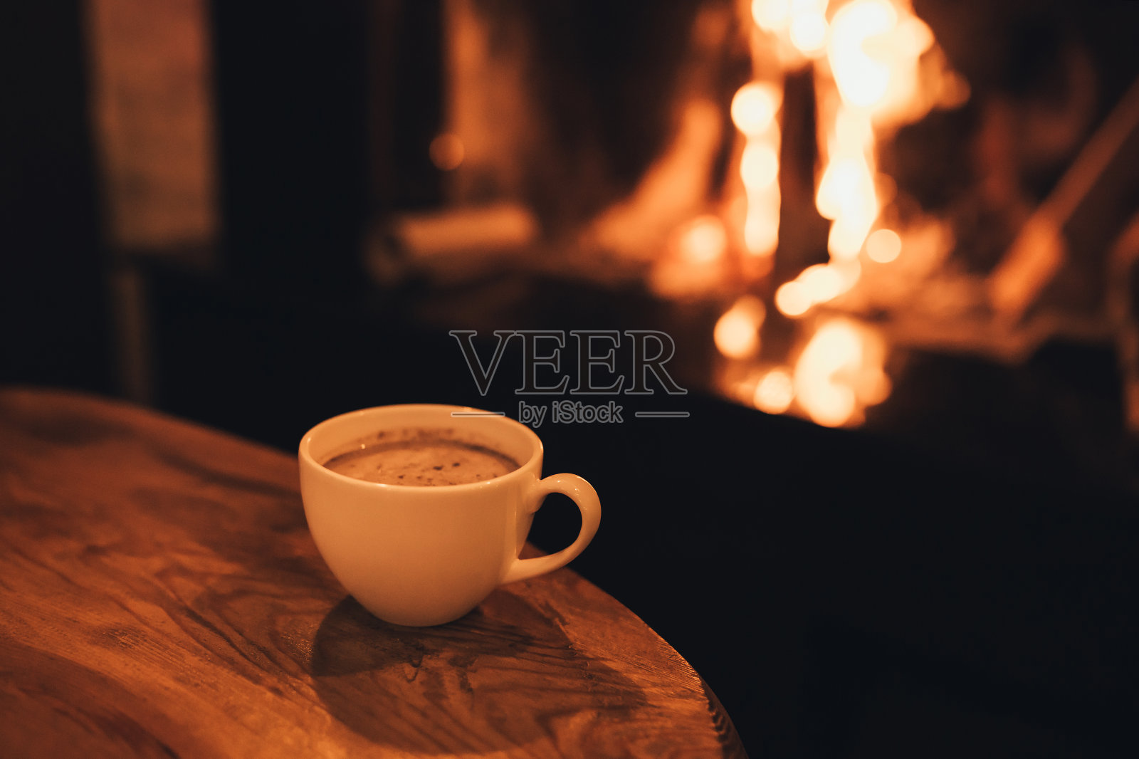 热巧克力在一个马克杯上的木制桌子与舒适的壁炉火焰的背景。照片摄影图片