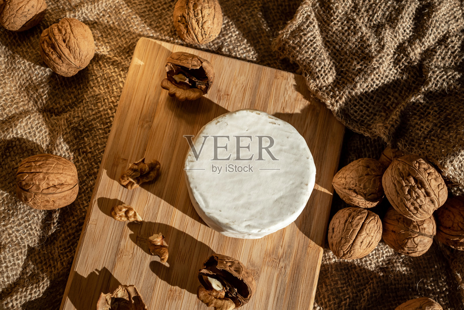 在粗麻布的背景上，一个圆头的奶酪与白色的模具和核桃在竹板上照片摄影图片