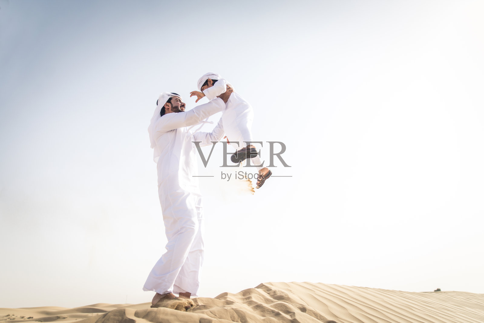 阿拉伯男子和儿子在沙漠中玩耍照片摄影图片