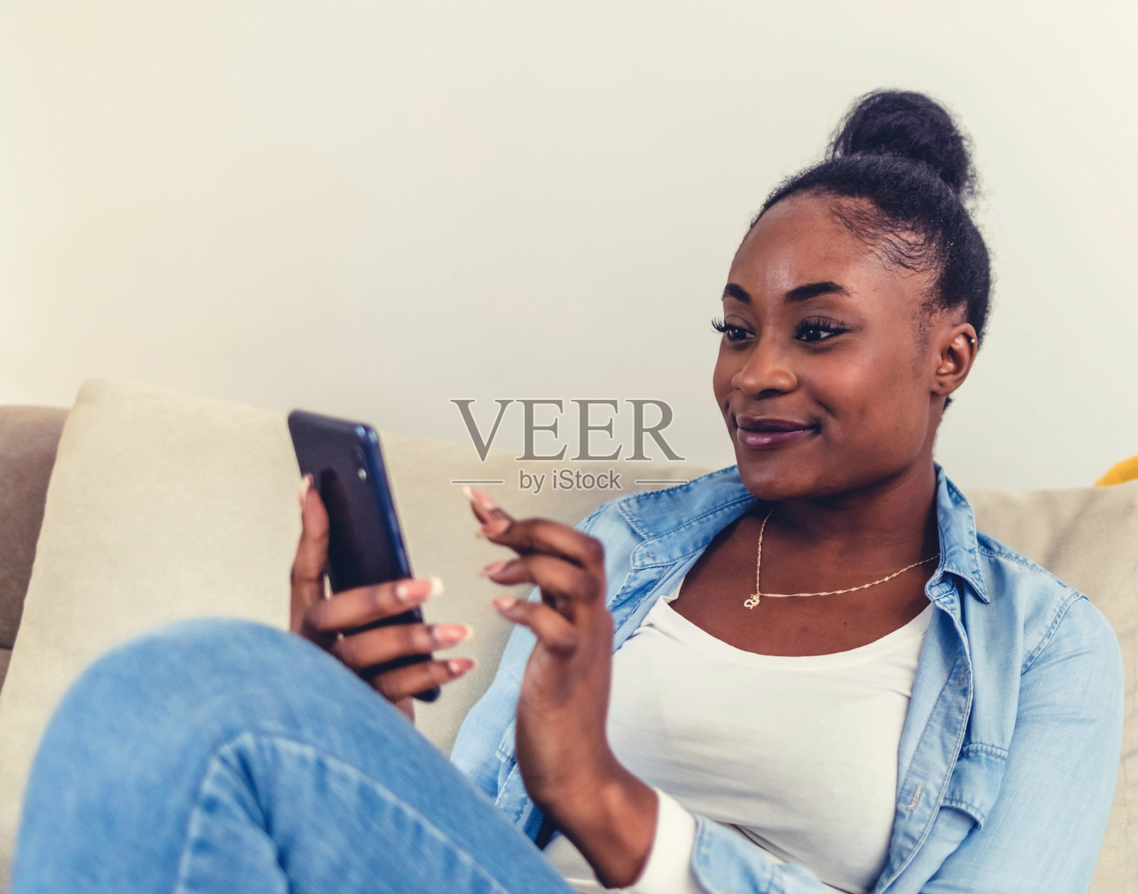 一个迷人的年轻女子独自坐在家里用手机发短信。照片摄影图片