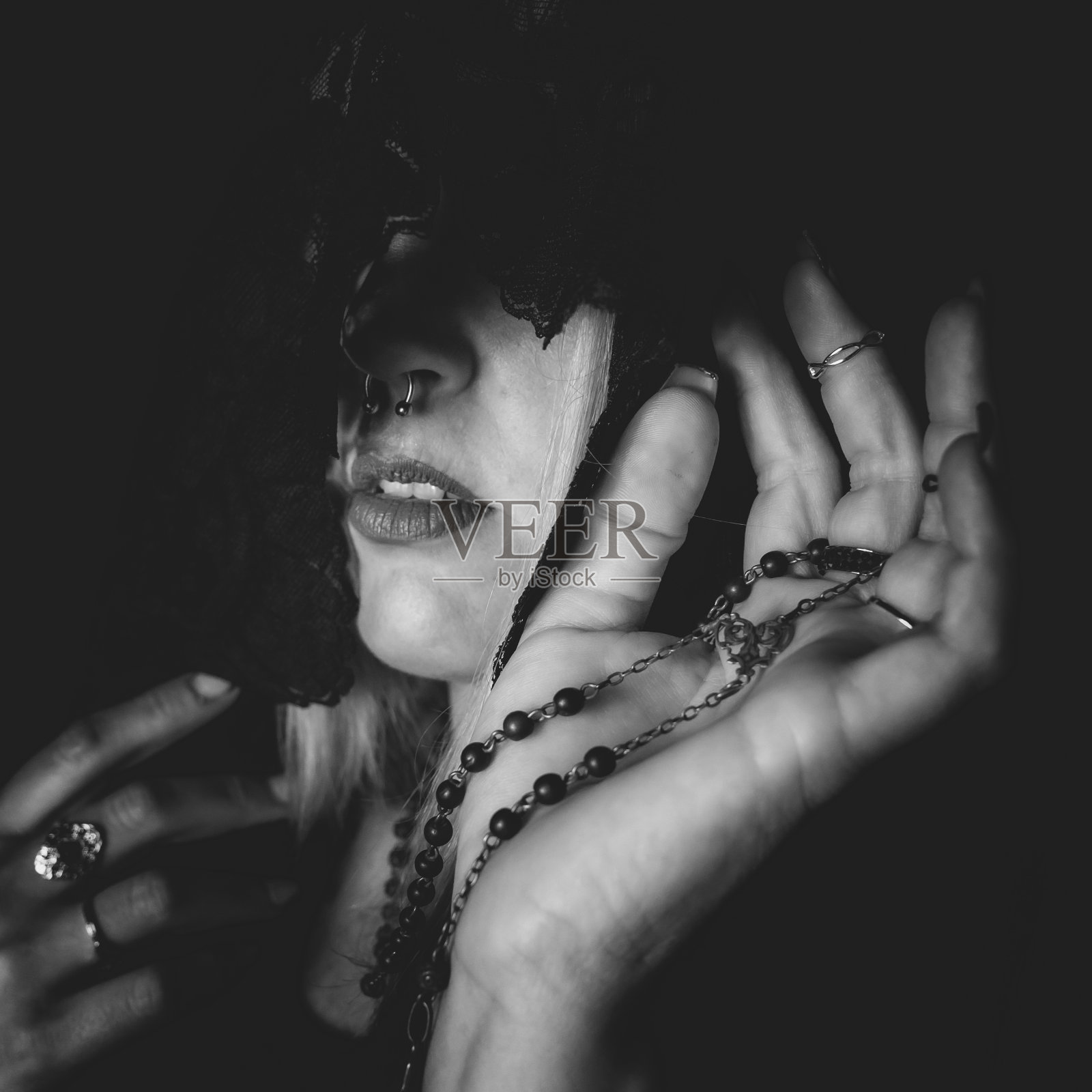 一个女人用灰色的镜头遮住脸，戴着许多戒指，拿着珠子照片摄影图片