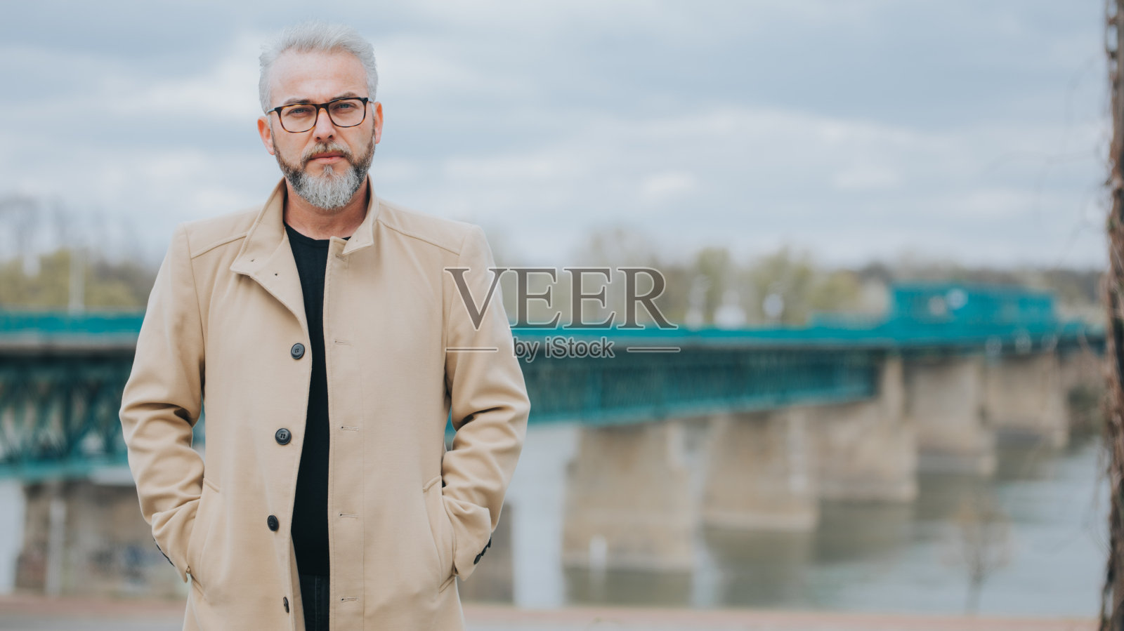 在桥的背景下，一个自信的灰发男人穿着时髦的棕色外套照片摄影图片