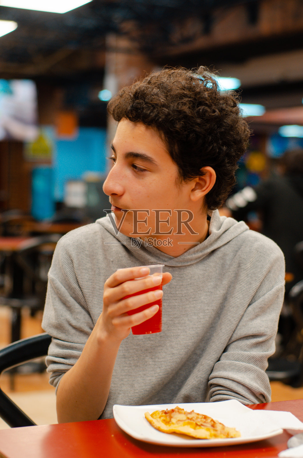 一个十几岁的男孩一边吃着披萨，一边喝着果汁照片摄影图片