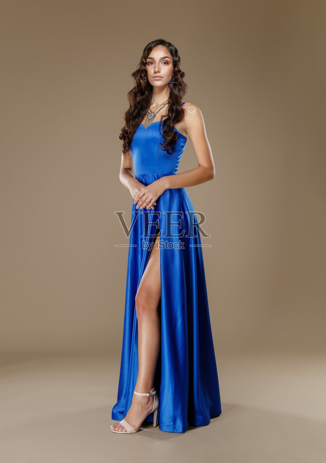 美丽的年轻女子在蓝色无袖及地长裙开叉看着镜头手牵手照片摄影图片