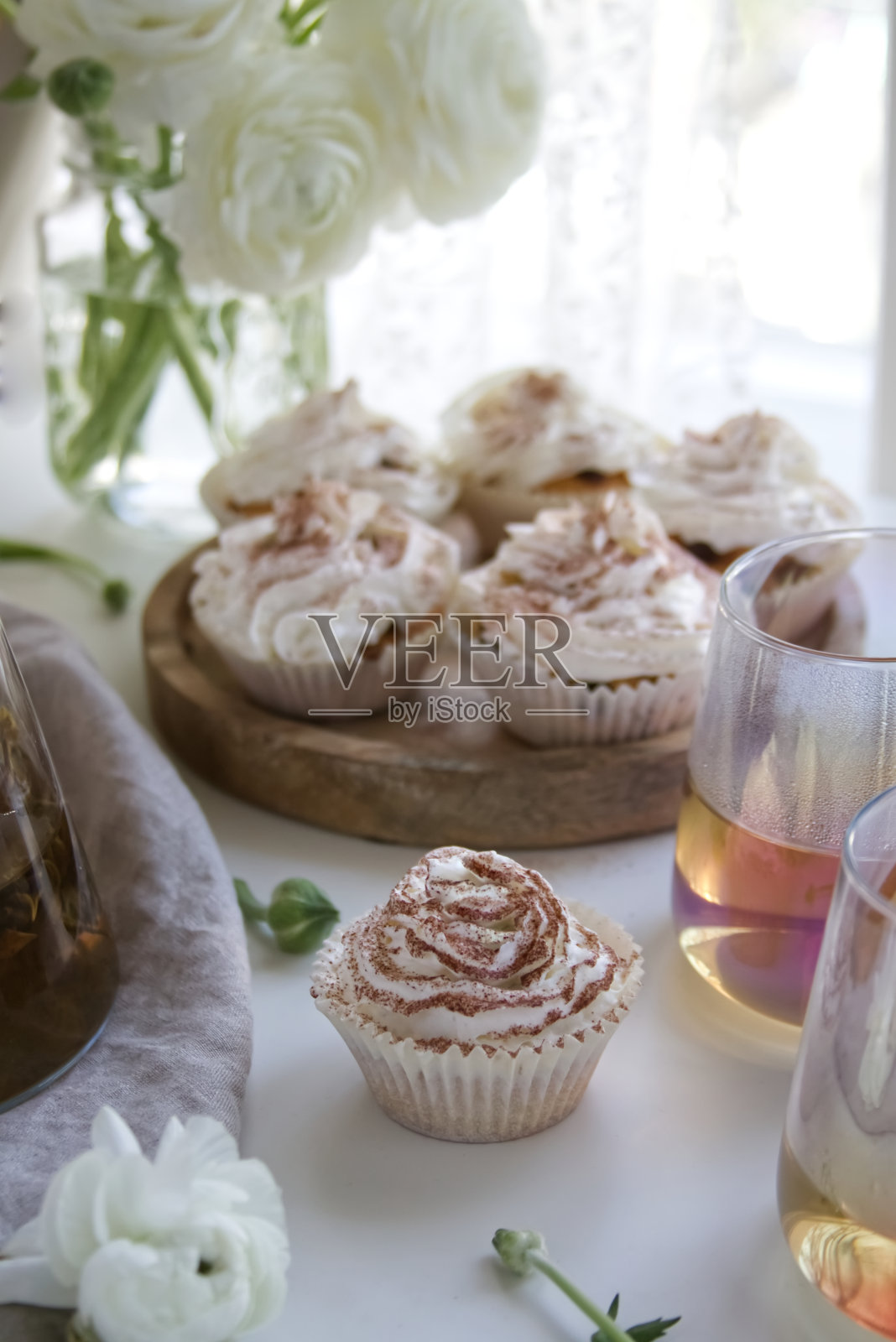 奶油和巧克力松饼放在木架上，旁边是白色的毛茛和一杯茶照片摄影图片
