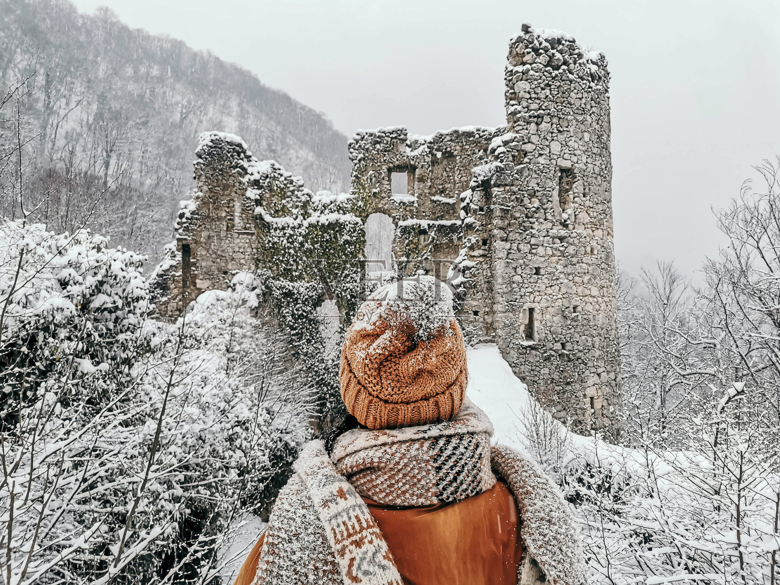 后视图的年轻女子在冬天的衣服。下雪了，看古堡废墟，户外，风格。照片摄影图片
