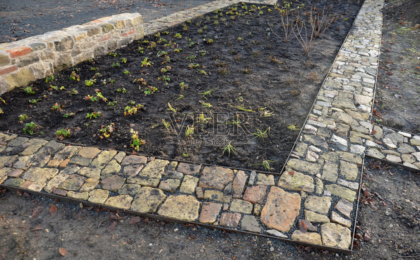石头路面刚刚铺干，在两个钢板路沿之间的砾石回填中。砂岩和烧过的砖块有一种乡村的感觉。草本花园里狭窄的公园小径，低矮，闭塞，烧焦了照片摄影图片