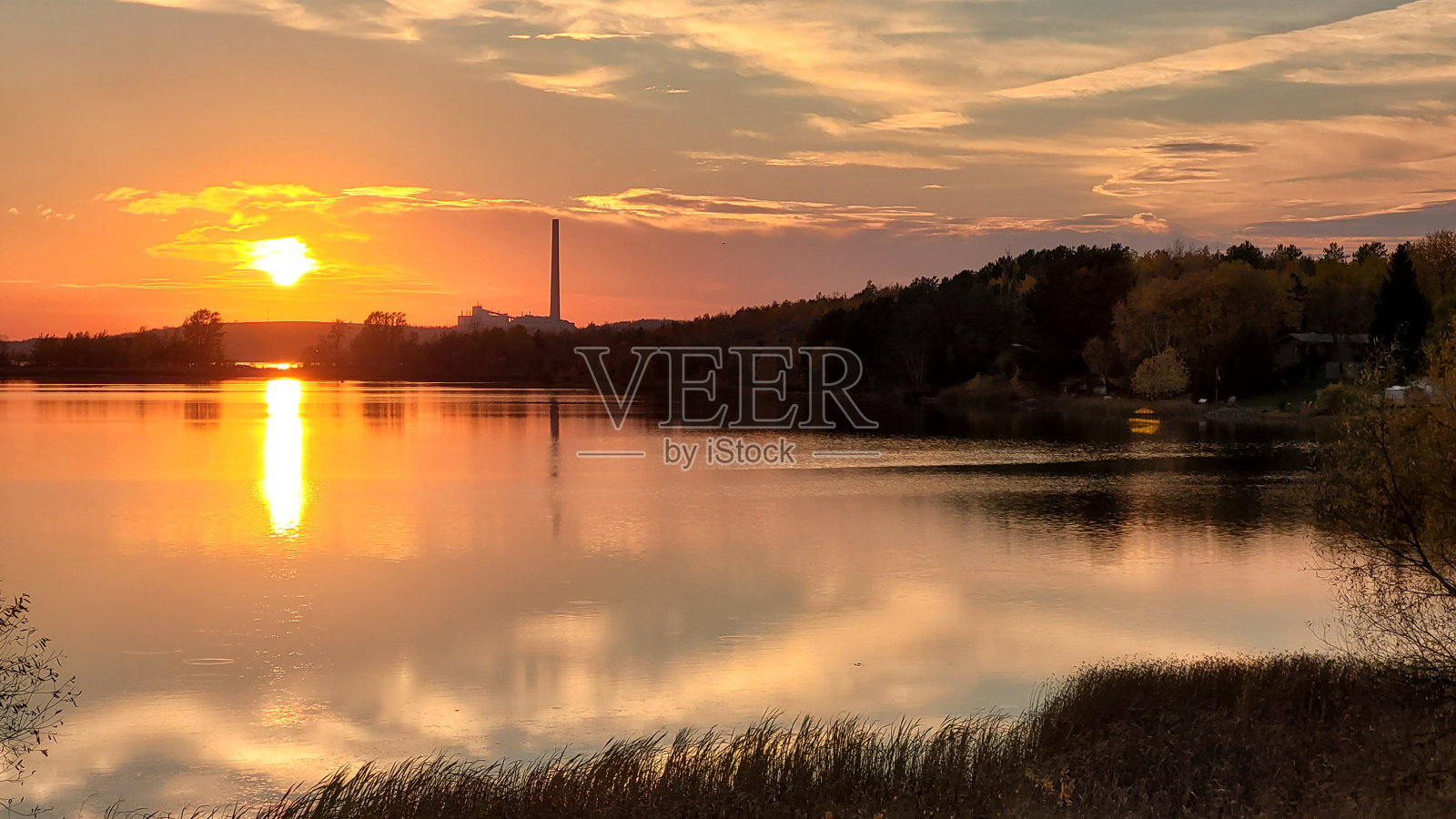 在一个湖的日落，一些树木装饰的景观，有一个塔在场景的背面，水看起来很安静照片摄影图片