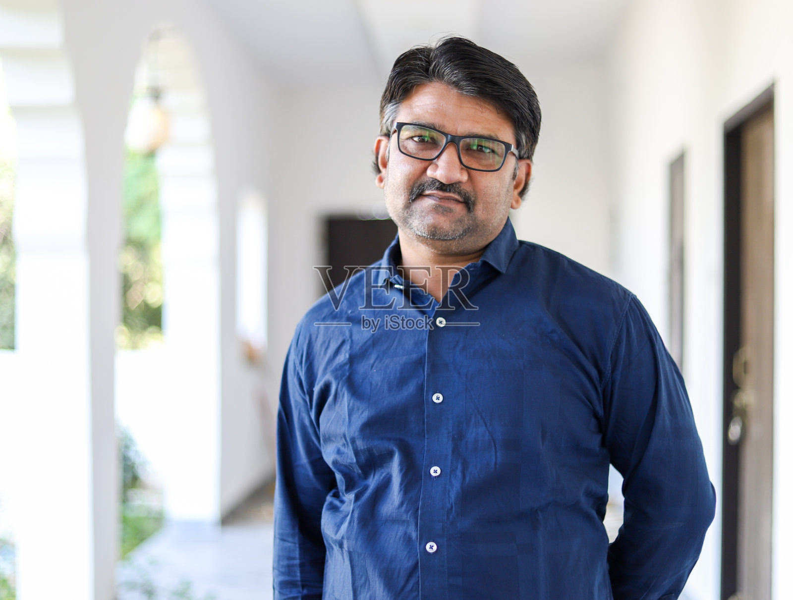 一个中年印度男子的肖像，戴眼镜，穿着蓝色衬衫照片摄影图片