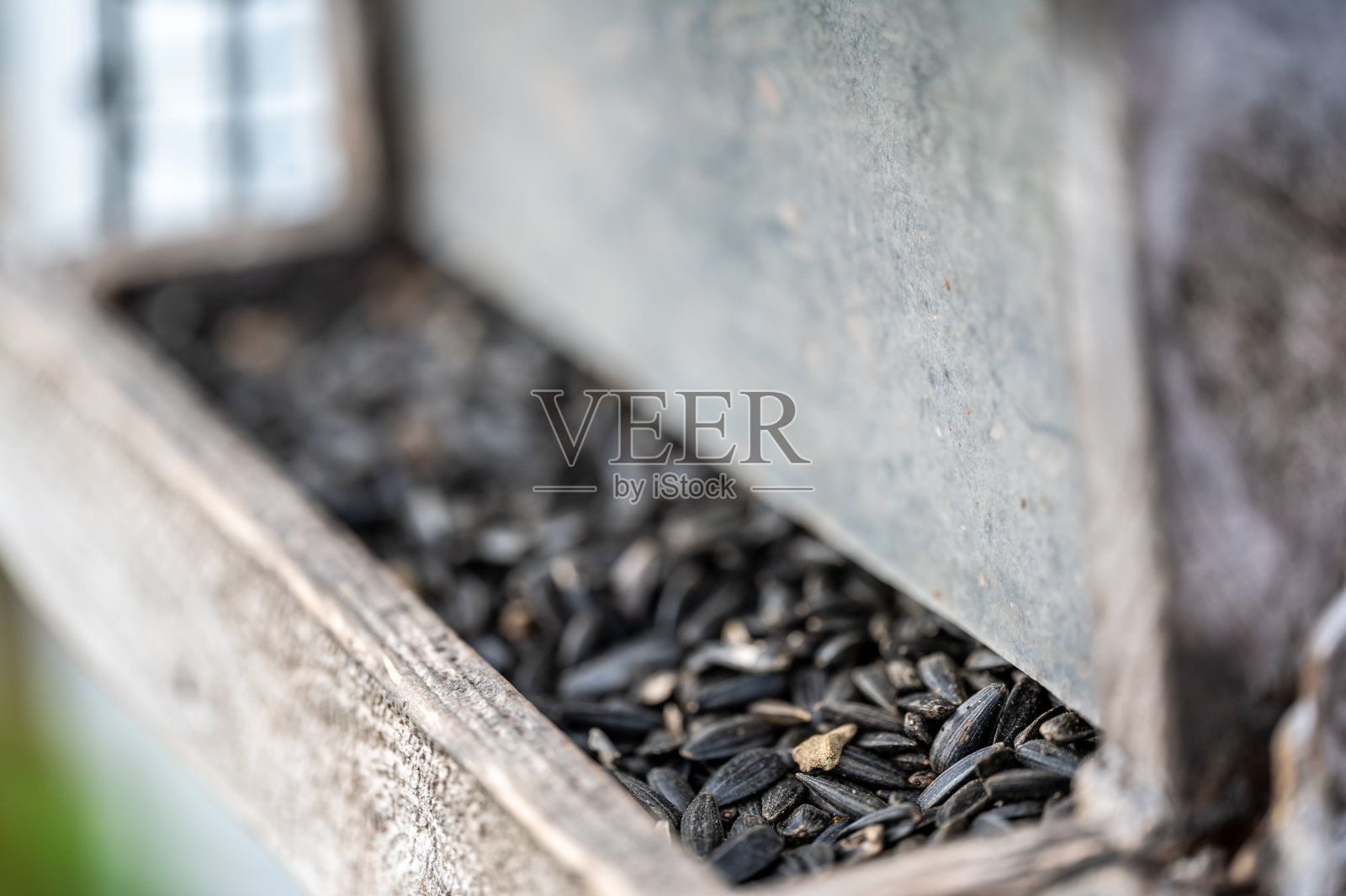 用葵花籽填充木制的饱经风霜的喂鸟器。照片摄影图片