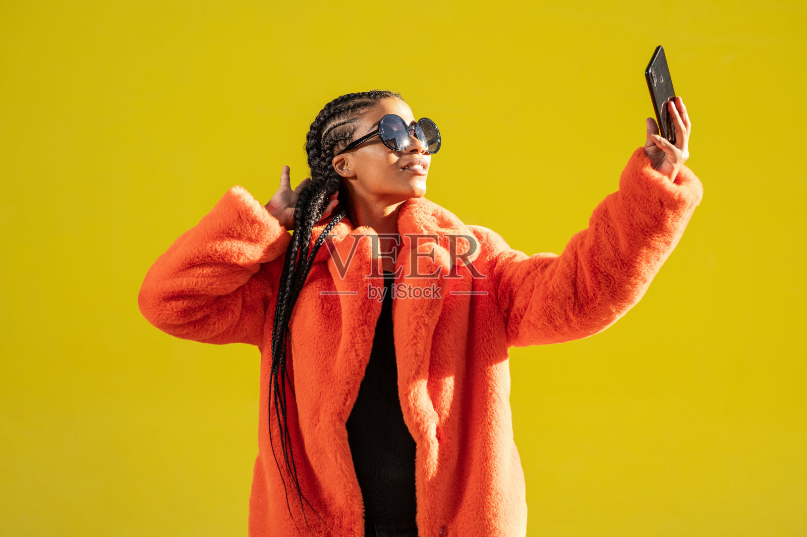 梳着非洲辫子、戴着墨镜的小女孩在黄墙前自拍照片摄影图片