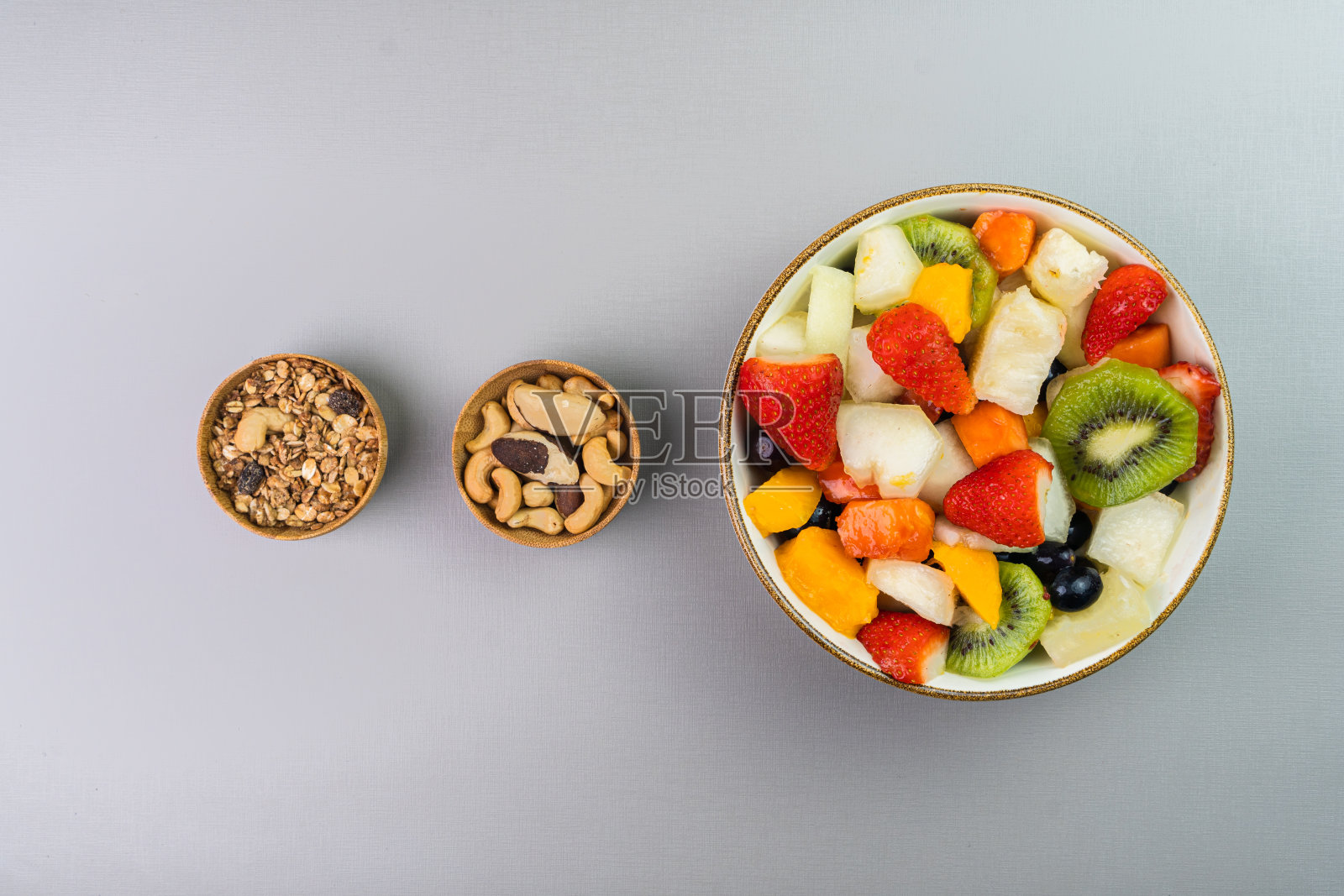 新鲜水果沙拉在碗里。多种颜色的热带水果。菠萝，芒果，葡萄，草莓，木瓜，瓜，猕猴桃。额外加入栗子和格兰诺拉麦片。前视图。有选择性的重点照片摄影图片