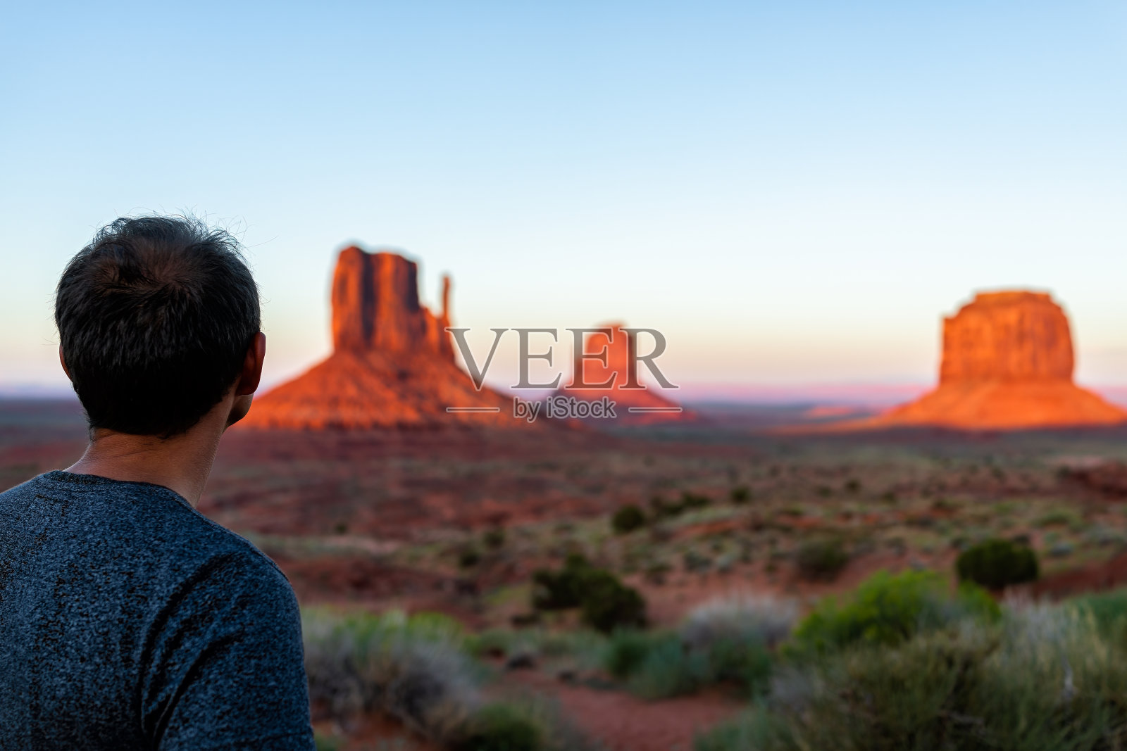 一名男子站在纪念碑谷的著名山峰的景色，在日落时，亚利桑那五颜六色的光，橘红色的岩石和植物照片摄影图片