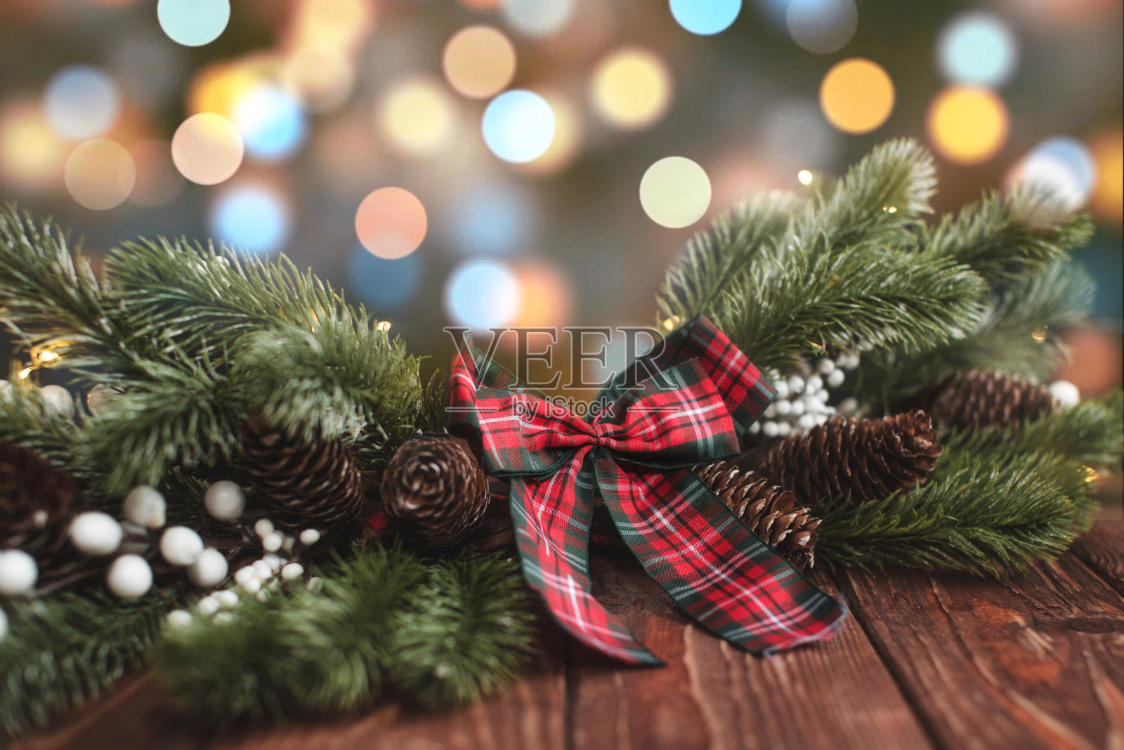 在模糊的灯光背景下，木制地板上有一棵带有凸起和蝴蝶结的圣诞云杉。照片摄影图片