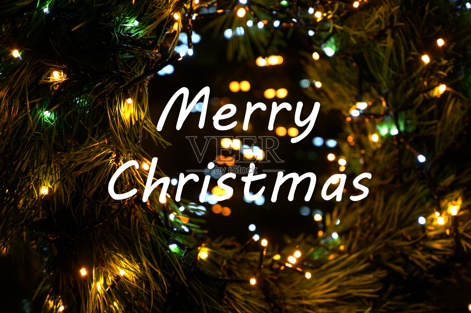 圣诞快乐的文字在冬天常绿的树枝上覆盖着雪与散景灯。照片摄影图片