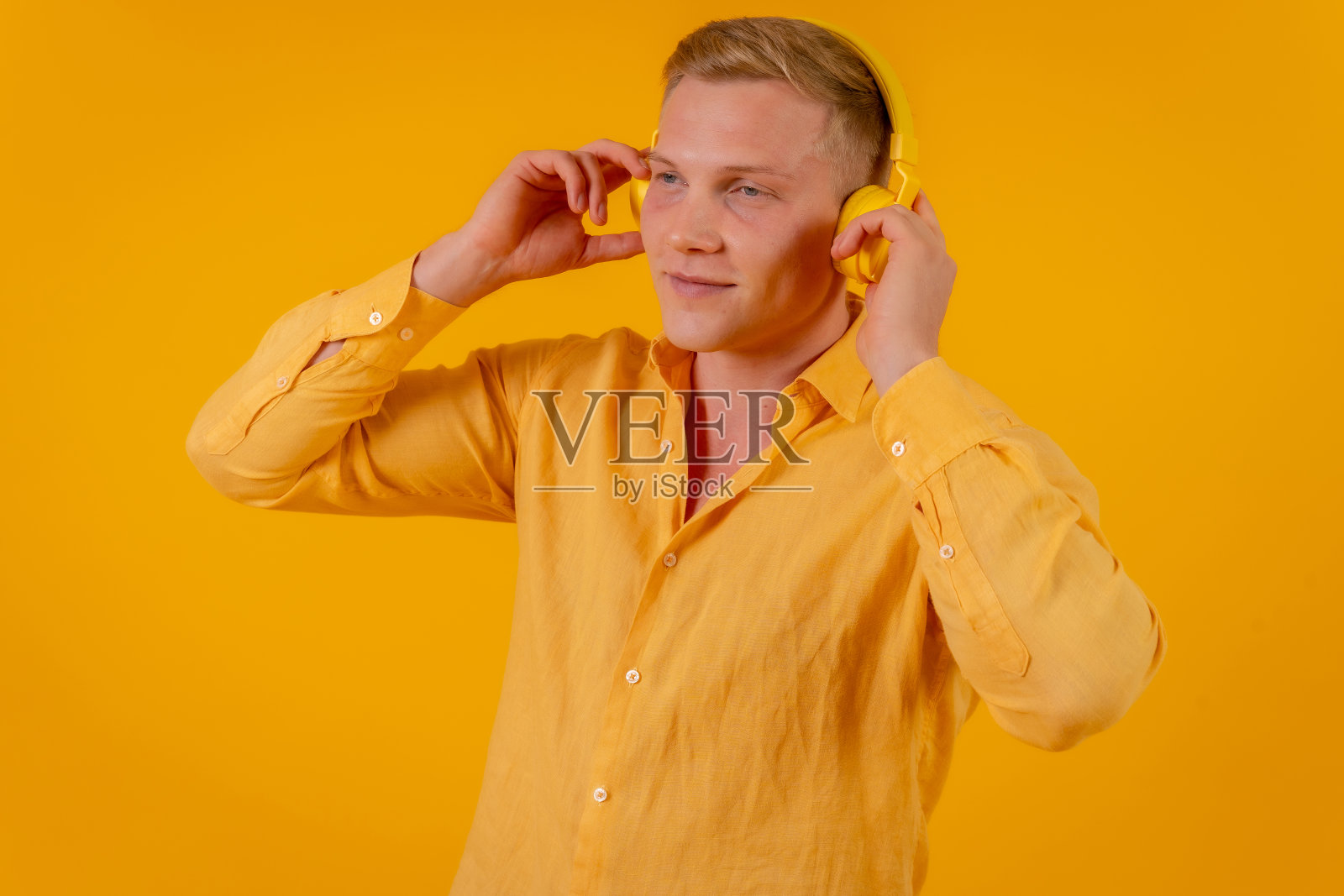 黄色背景的金发白人，戴着无线耳机听音乐照片摄影图片