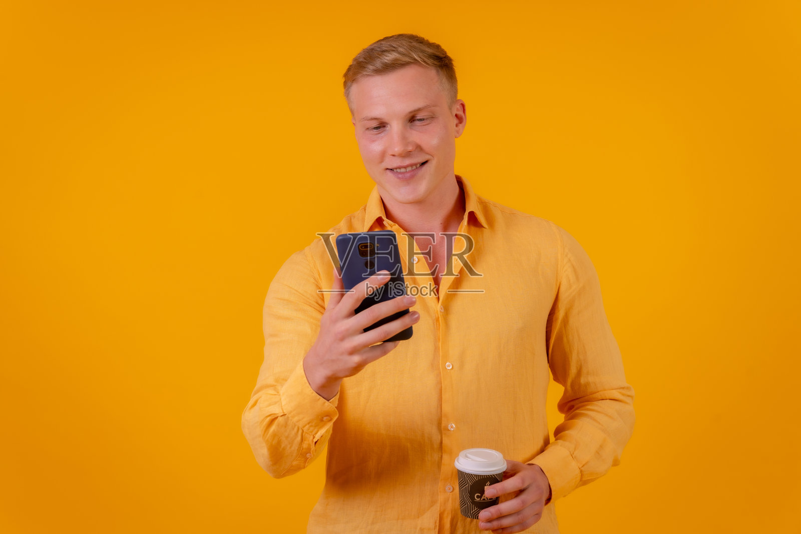 黄色背景的金发白人男子，在用手机照片摄影图片