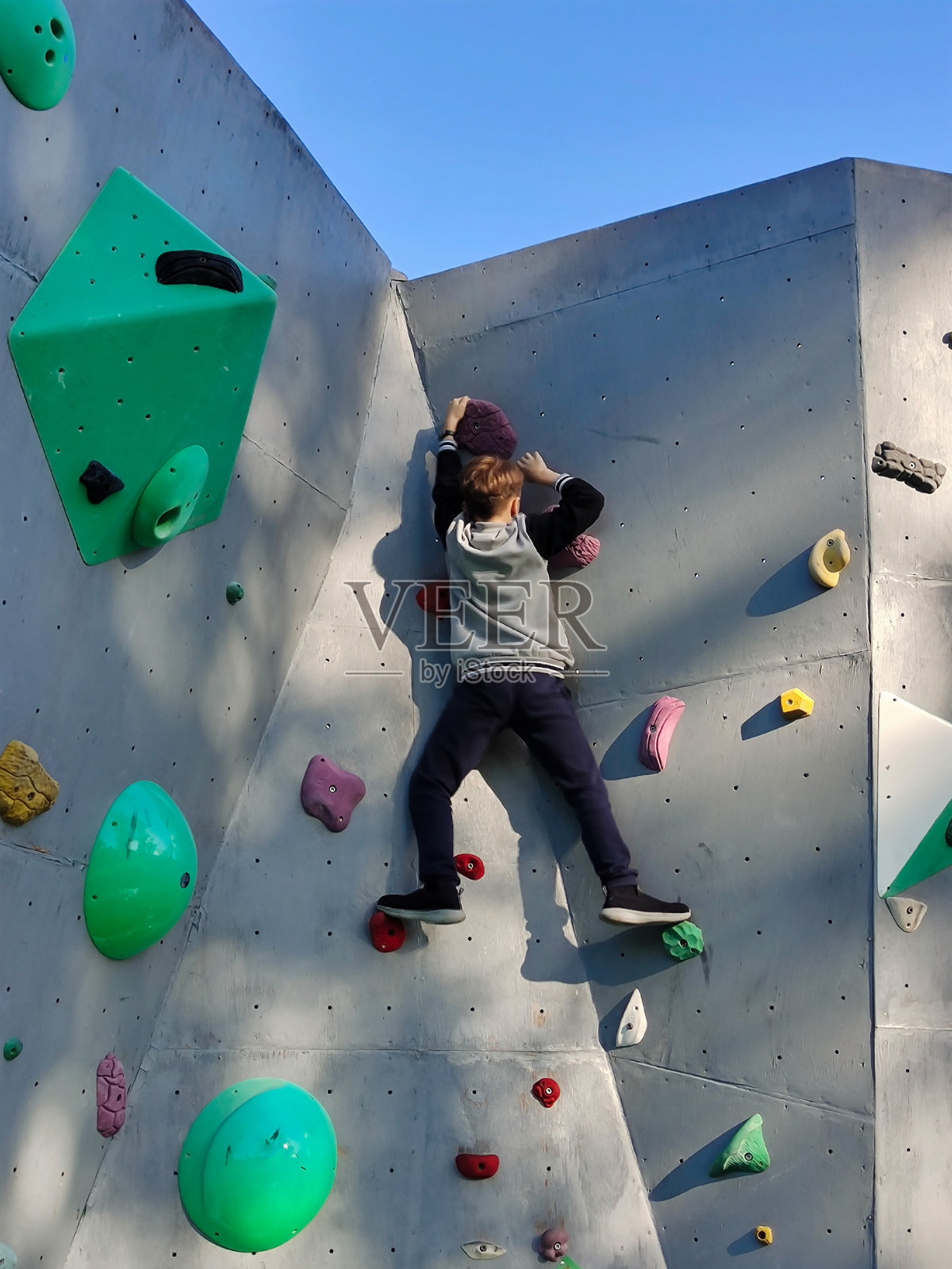 一个十几岁的男孩爬上墙去爬钩子。从下面看照片摄影图片