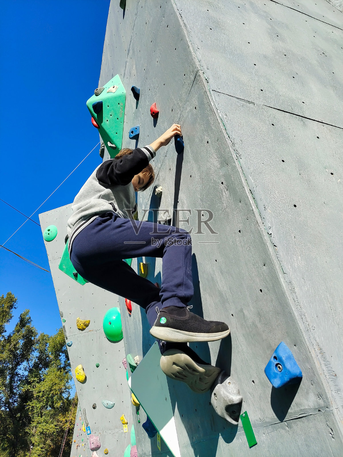 一个十几岁的男孩爬上墙去爬钩子。从下面看照片摄影图片