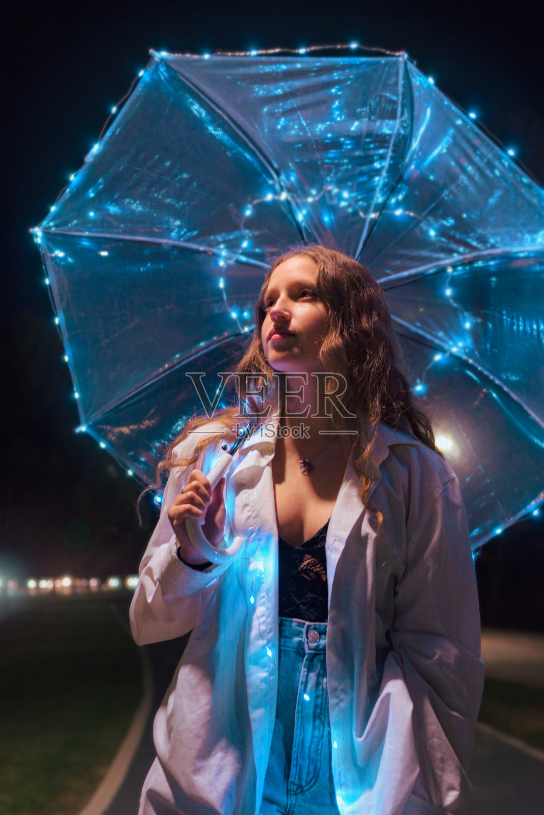 年轻女子在夜晚带着灯走在伞下照片摄影图片