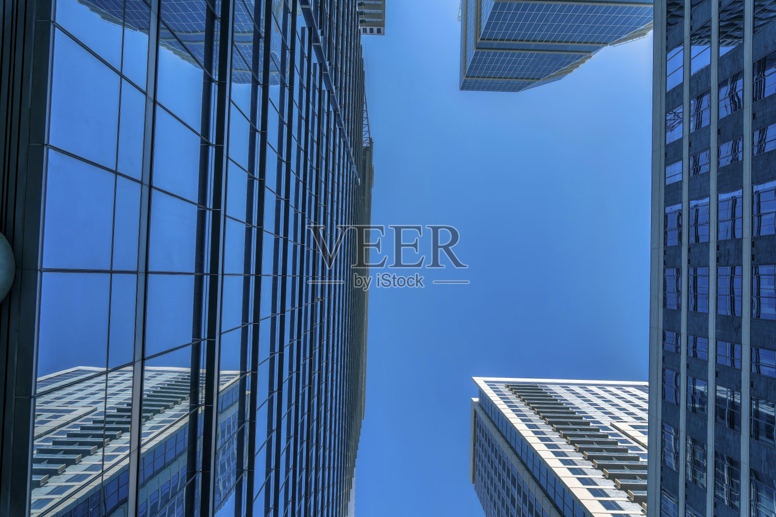 从现代玻璃建筑底部看，以蓝天为背景照片摄影图片